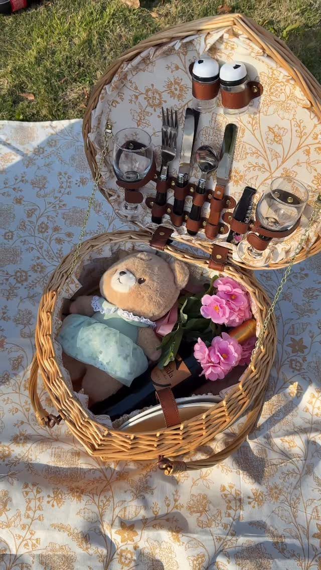 Wicker picnic basket containing a teddy bear and flowers on a floral blanket
