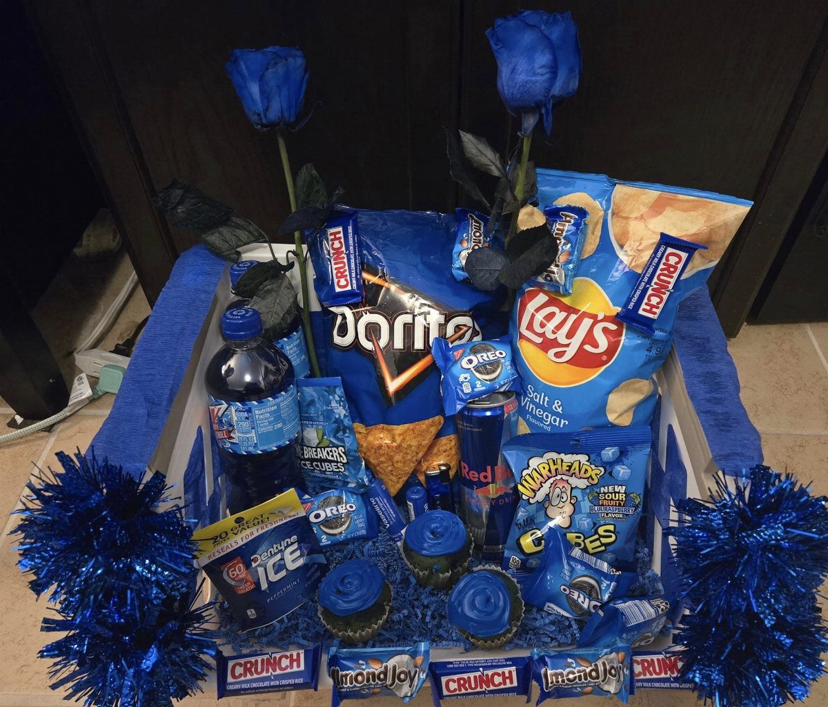 Blue-themed gift basket filled with chips, candy, soda, and blue roses.