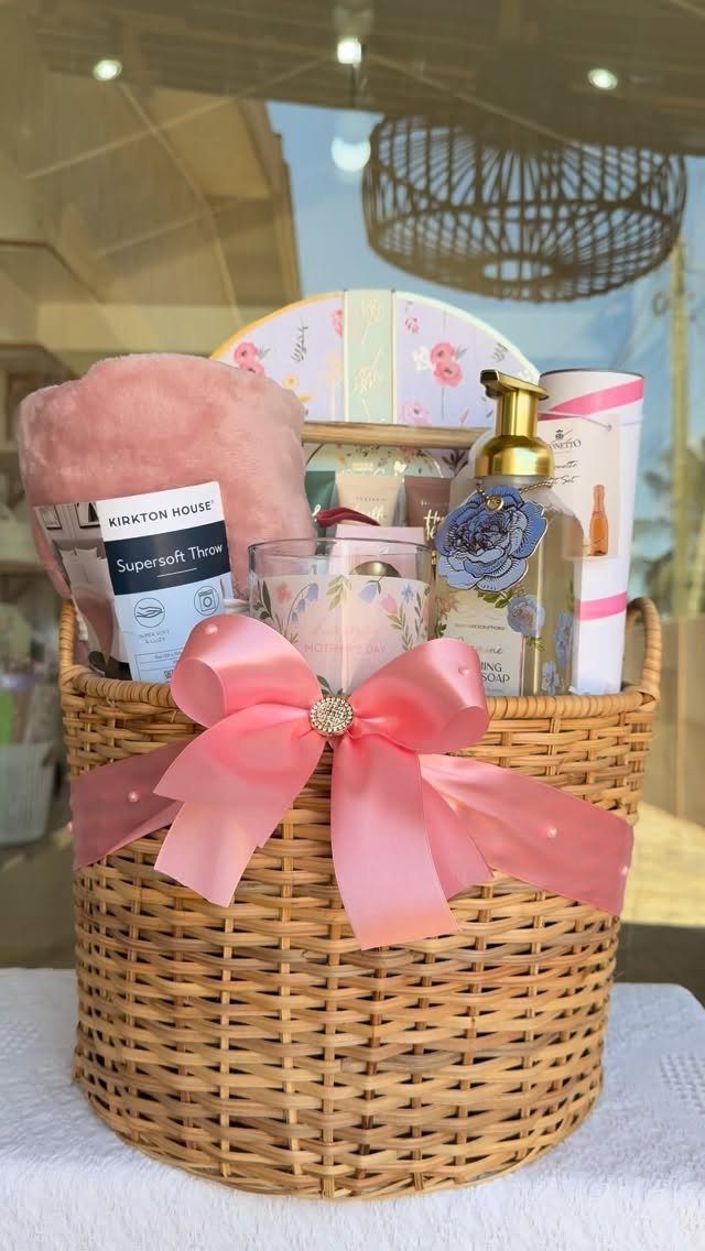 Woven wicker spa gift basket with pink bow, lotions, and plush accessories.