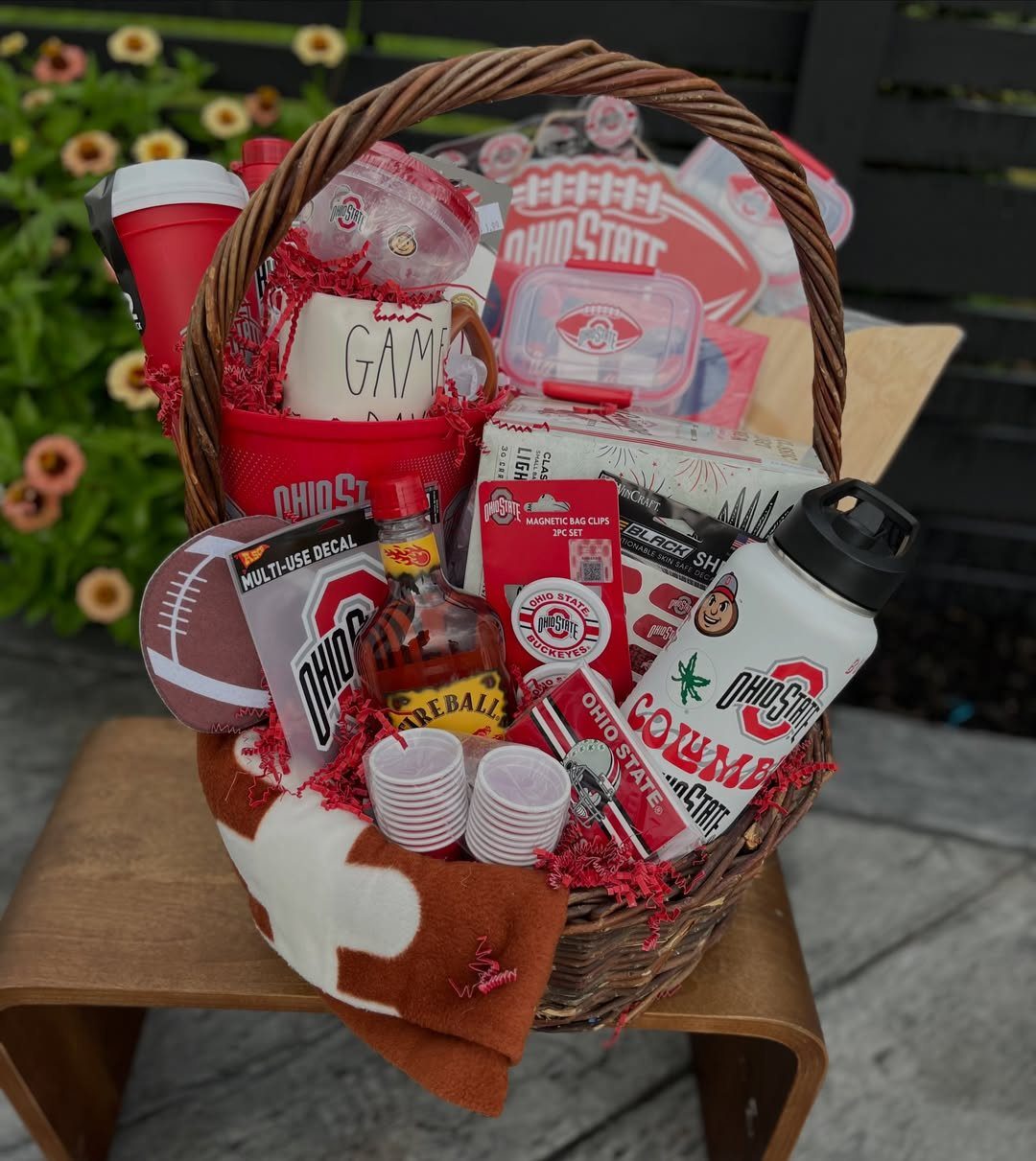 Ohio State themed gift basket with football, whiskey, and university merchandise on wooden stool.