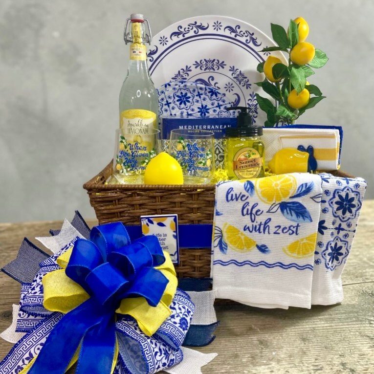 Wicker gift basket with lemons, blue and white Mediterranean plates, and lemon-themed towels.