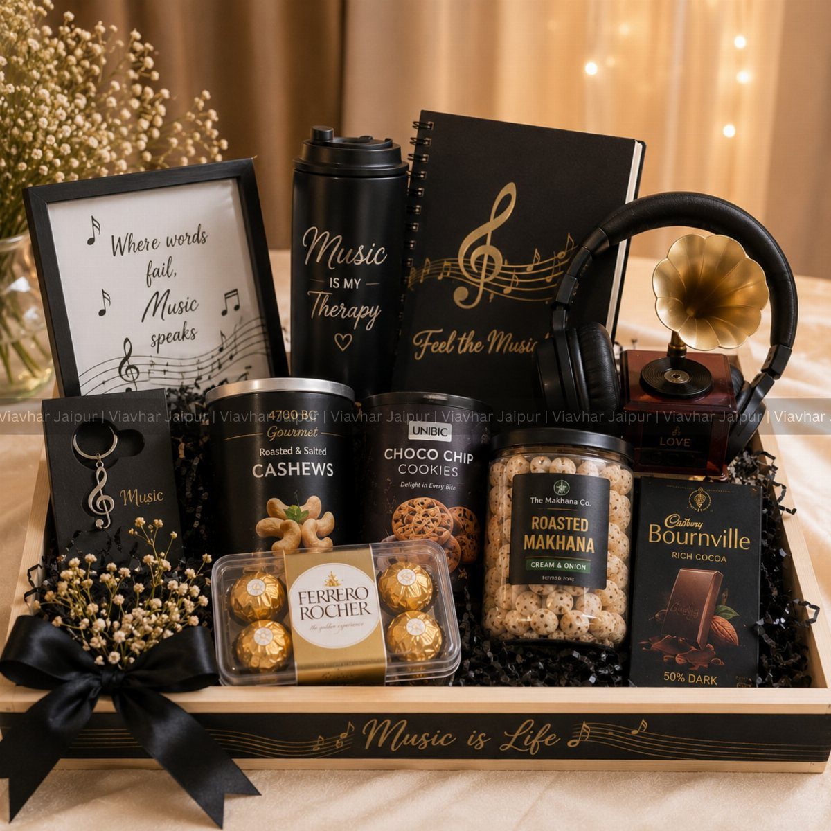 Music themed gift basket with black accessories, chocolates, and snacks in a wooden tray.