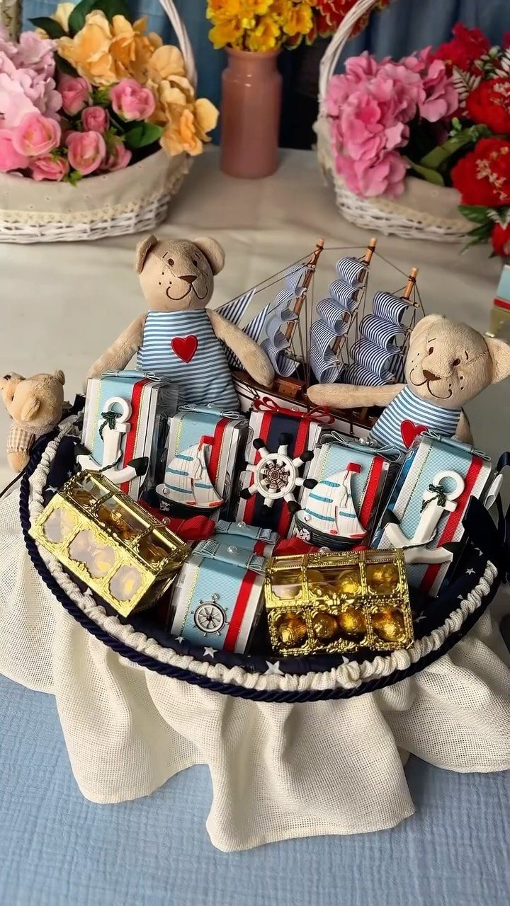 Nautical gift basket with teddy bears, a model sailboat, and anchor-themed wrapped presents.