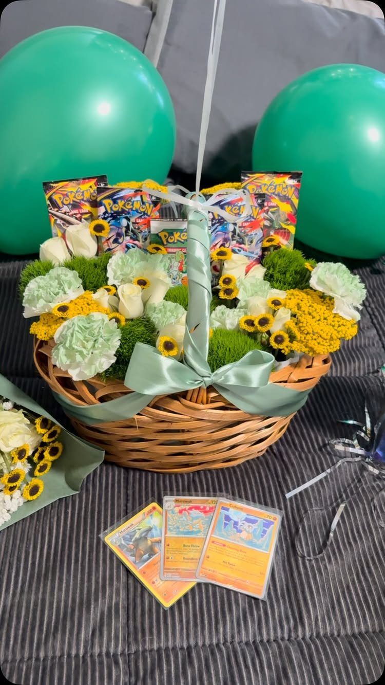 Wicker gift basket with yellow and white flowers, Pokemon cards, and green balloons.