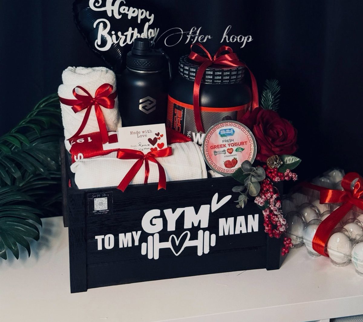 Fitness gift basket in a black crate with towels, water bottle, and supplements.