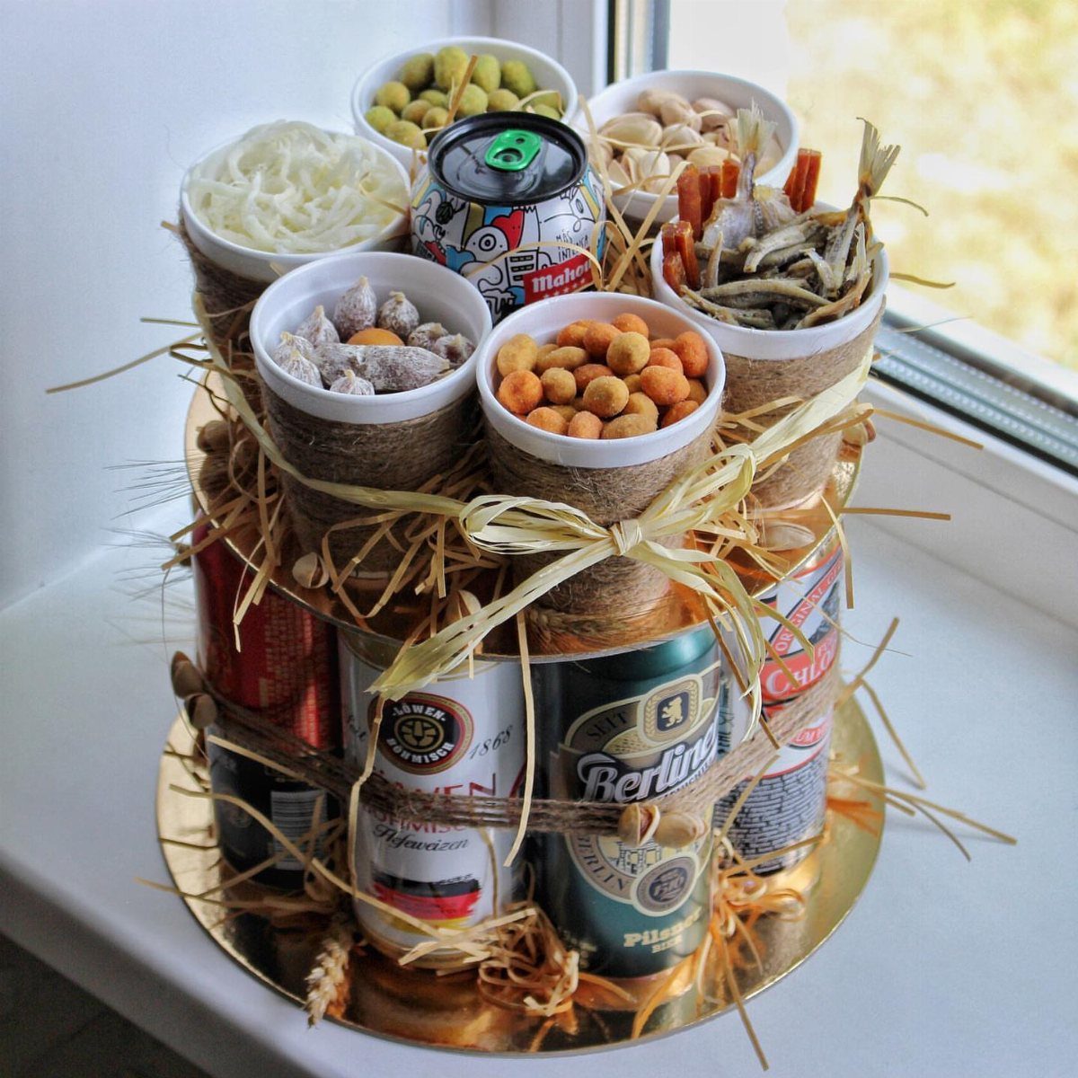 Beer cans and snack bowls arranged in a tiered gift basket with straw.