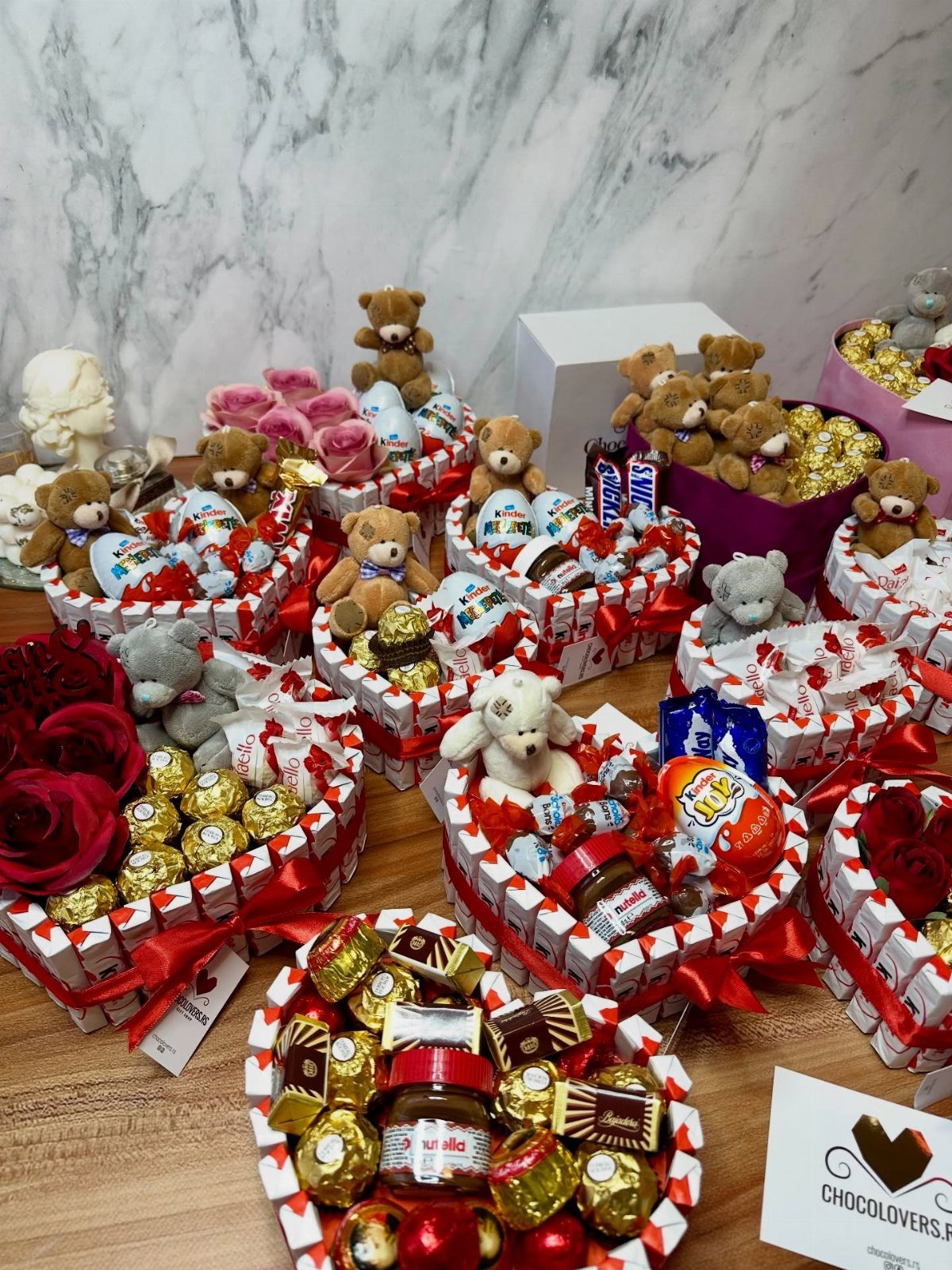 Heart-shaped gift baskets filled with chocolates, candies, teddy bears, and red roses.