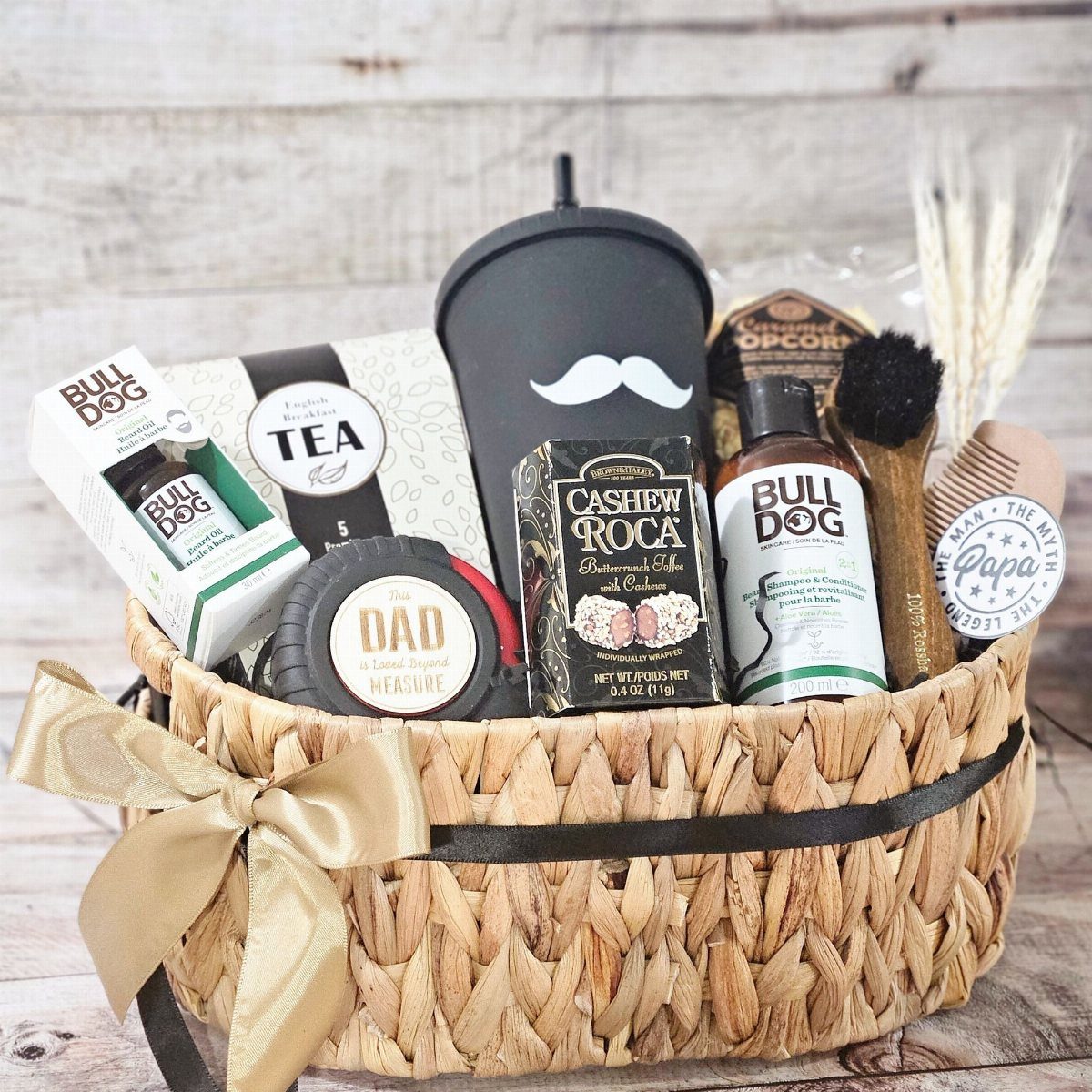Woven gift basket with grooming products, snacks, and a black mustache tumbler.