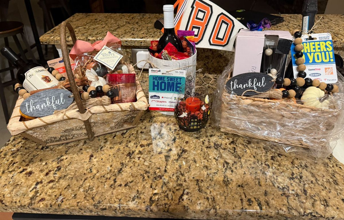 Three wine gift baskets with autumn decorations and treats on a granite counter