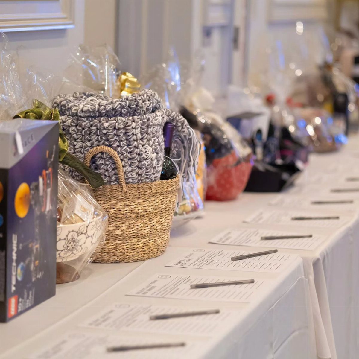 Gift baskets wrapped in cellophane on a white table for a raffle event