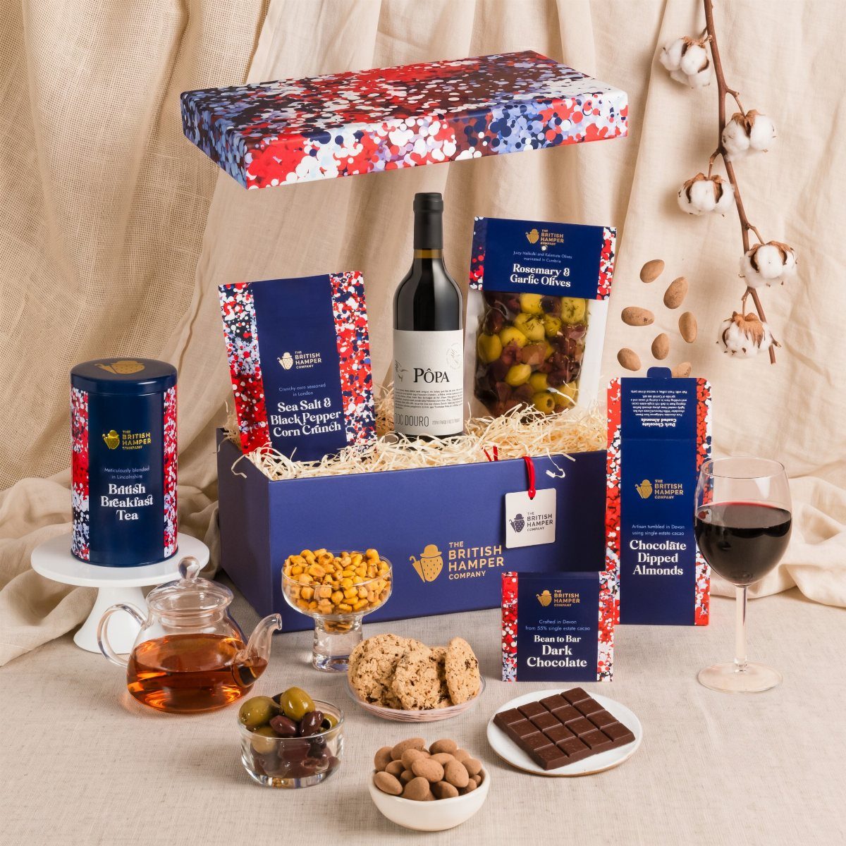 Wine gift box with gourmet snacks, olives, chocolate, and a glass of red wine.