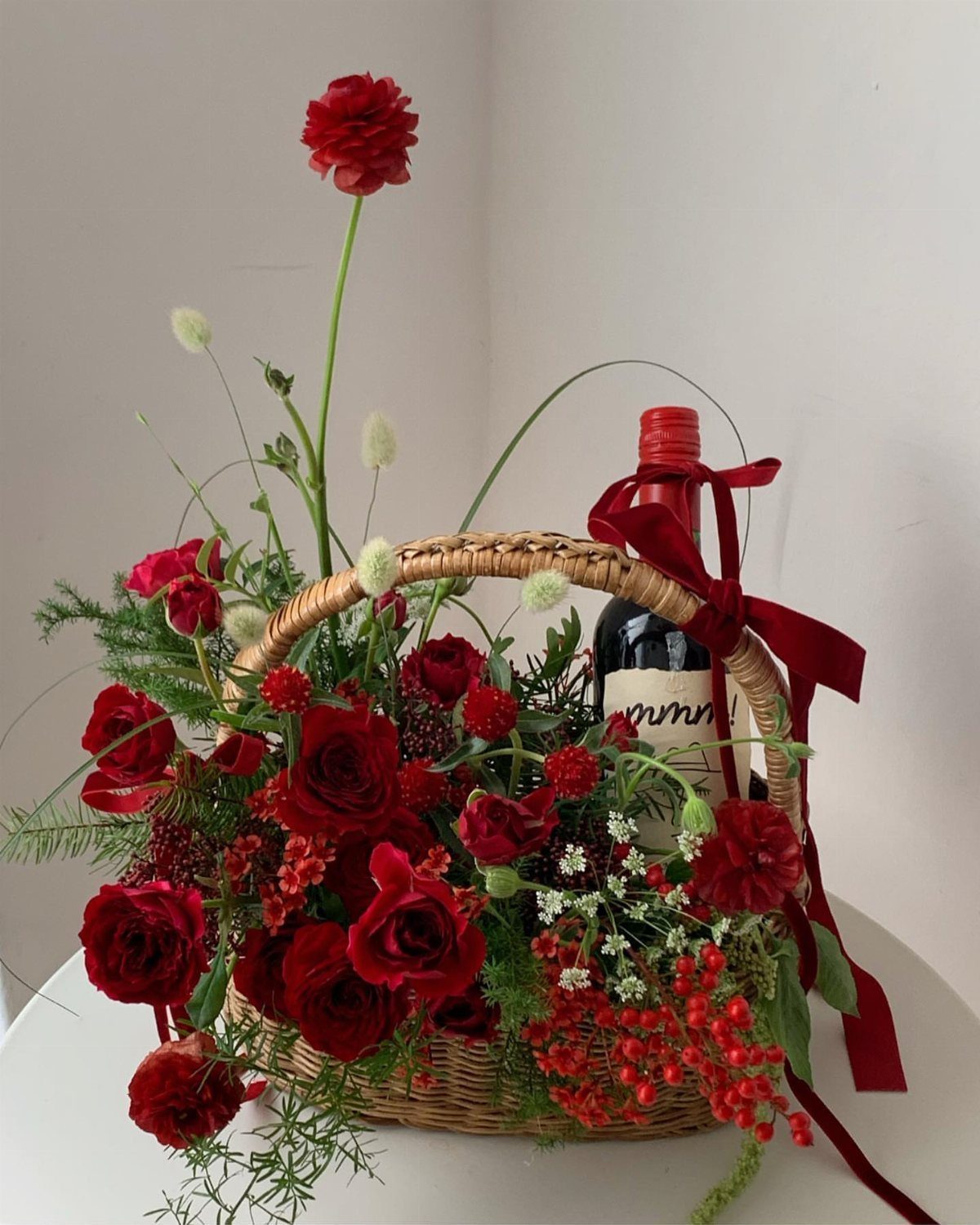Wicker basket with a bottle of red wine and red rose floral arrangement.