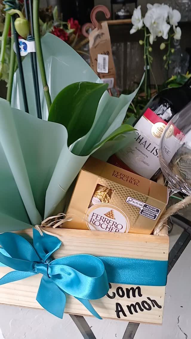 Wooden gift crate with wine, Ferrero Rocher chocolates, and a blue satin bow.