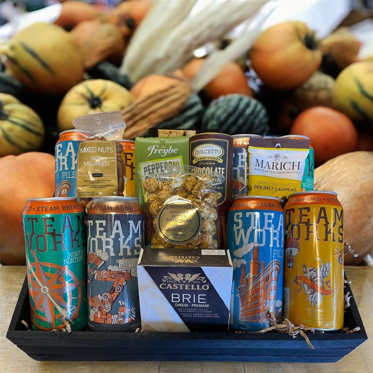 Craft beer gift basket with colorful cans, gourmet snacks, and brie cheese.
