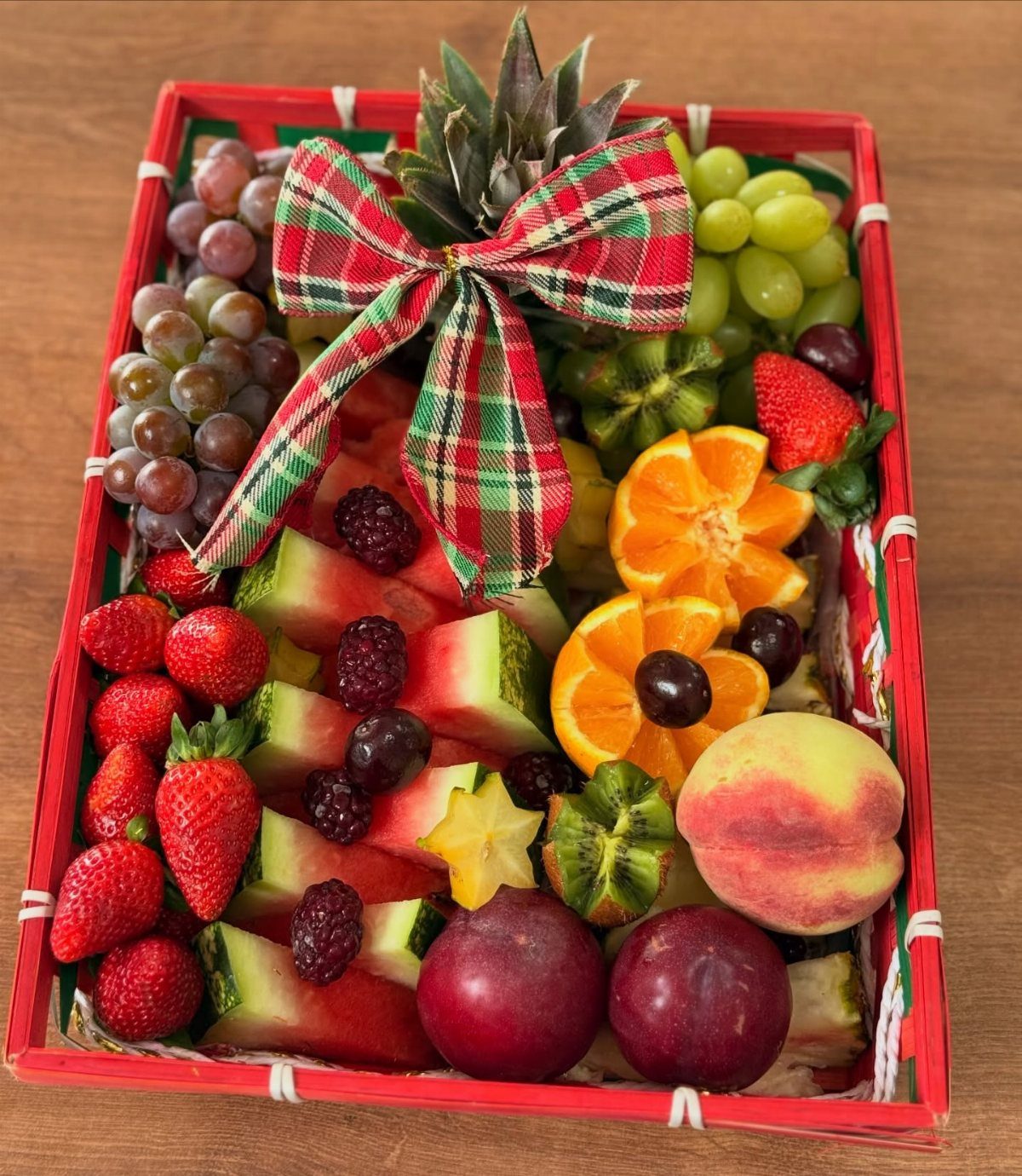Fruit basket with red and green grapes, strawberries, and watermelon tied with plaid bow.