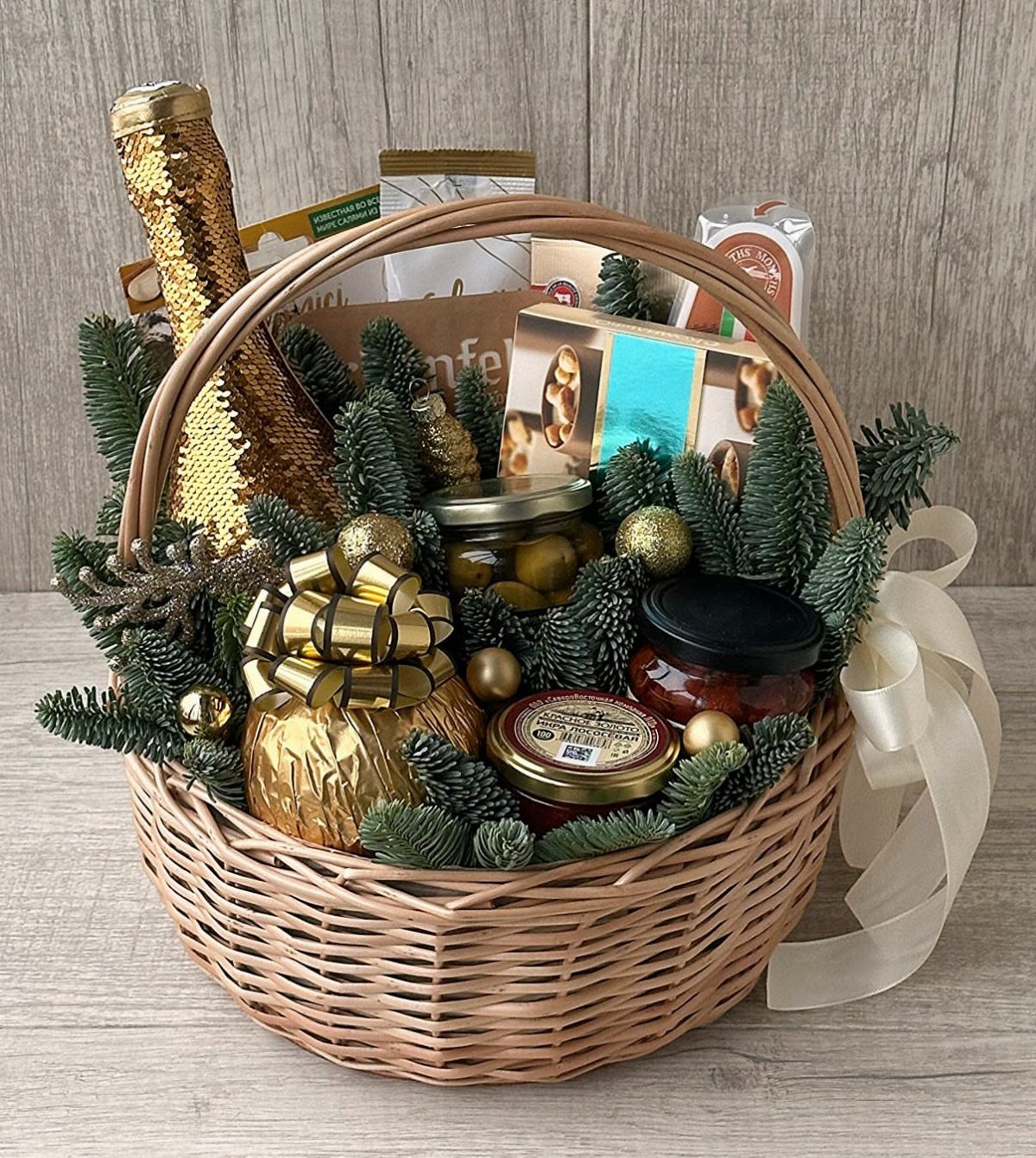 Woven gift basket filled with gourmet treats, gold bottle, and pine decorations.