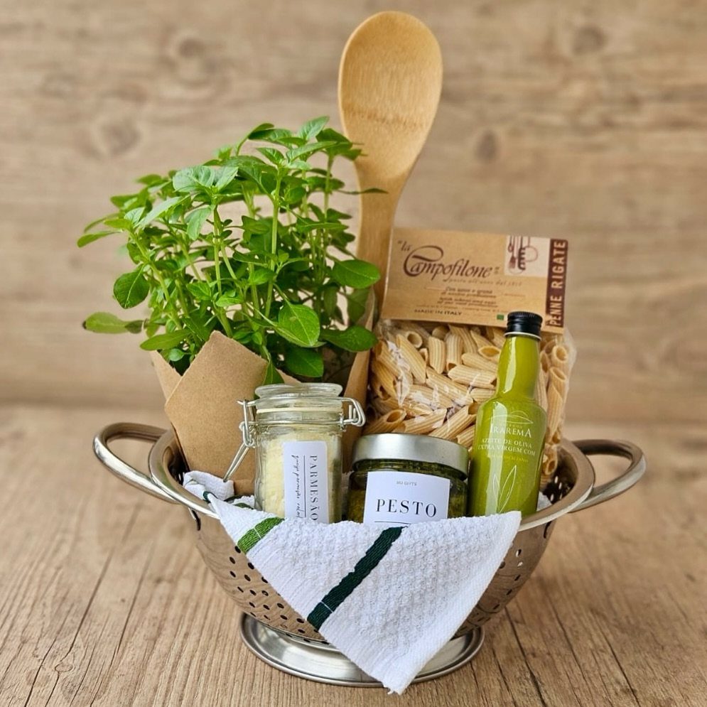 Pasta gift basket in a metal colander with pesto, oil, and fresh basil.